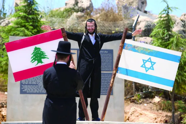 إسرائيلي متشدد يلتقط صورة قرب عَلَمَي لبنان وإسرائيل مرفوعين على نصب تذكاري في بلدة المطلة المحاذية للحدود اللبنانية (أرشيفية - أ.ب)