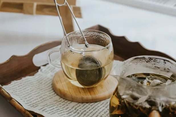 كوب شاي دافىء مع مصفاة يظهر على صينية من خشب (بيكسلز)
