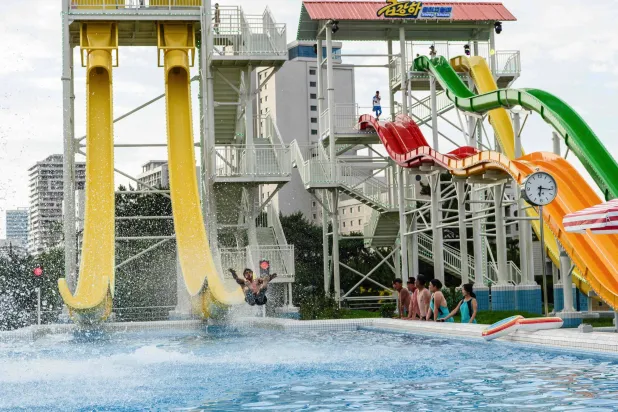 (FILES) Domestic tourists watch as a man uses a slide into a swimming pool at the Myongsasimni Water Park in the Wonsan Kalma Coastal Tourist Area in Wonsan, North Korea's Kangwon Province on July 2, 2025. (Photo by KIM Won Jin / AFP)