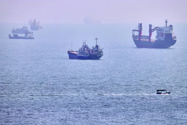 Bender Abbas açıklarında, Hürmüz Boğazı'nda demirlemiş kargo gemileri ve ticari tankerlerin yakınında küçük bir tekne seyrediyor (AP)
