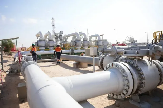 Workers walk across pipelines at the Rumaila oil field in Basra, Iraq (Reuters)