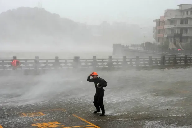  In this photo released by Xinhua News Agency, a man walks against strong wind and rain as Typhoon Dolphin makes landfall at Dongsha community in Yuhuan, Taizhou, eastern China's Zhejiang Province on Sunday, Aug. 9, 2026. (Xinhua via AP) 