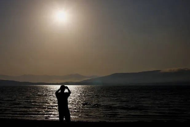 A tourist photographs the sun with his mobile phone at Arija beach, Spain, August 11, 2026. (Reuters)