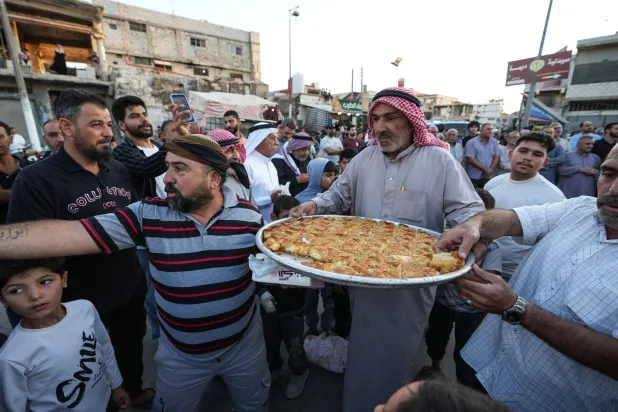 سوريون يوزّعون الحلويات خارج المسجد العمري في درعا البلد احتفالاً بالحكم على عاطف نجيب رجل أمن الأسد الذي ارتكب جرائم بحق الأهالي (د.ب.أ)