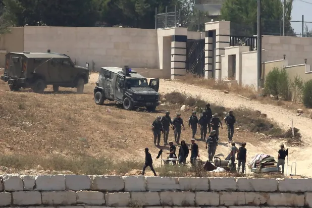 جنود إسرائيليون يقفون حراساً بجوار مستوطنين أمام منازل فلسطينية حاصروها في قرية قصرة جنوب نابلس بالضفة الغربية المحتلة (أ.ب)
