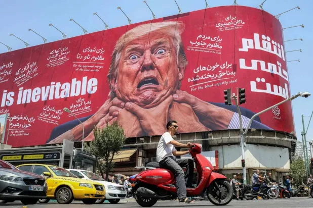 A woman walks past a large billboard pledging revenge against US President Donald Trump along Jomhouri Street in central Tehran on July 27, 2026. (AFP)