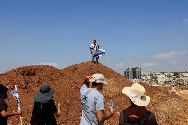 Armed Israeli settlers holding an Israeli flag look on as Palestinian and Israeli activists accompany Palestinian landowners in their property, which is threatened with confiscation by Israeli settlers, in Beit Sahour in the Israeli-occupied West Bank August 14, 2026. REUTERS/Mussa Qawasma

