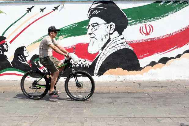 An Iranian man passes with his bike next to a wall painting featuring slain Iranian supreme leader Ali Khamenei in a street in central Tehran, Iran, 13 August 2026. (EPA)