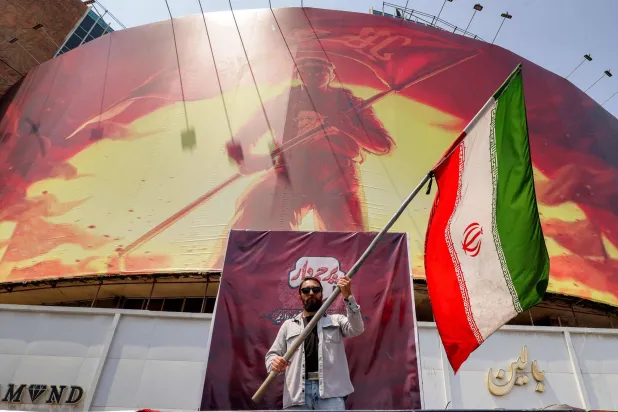 A man waves an Iranian flag before a political billboard at Valiasr Square in central Tehran on August 8, 2026. (AFP)
