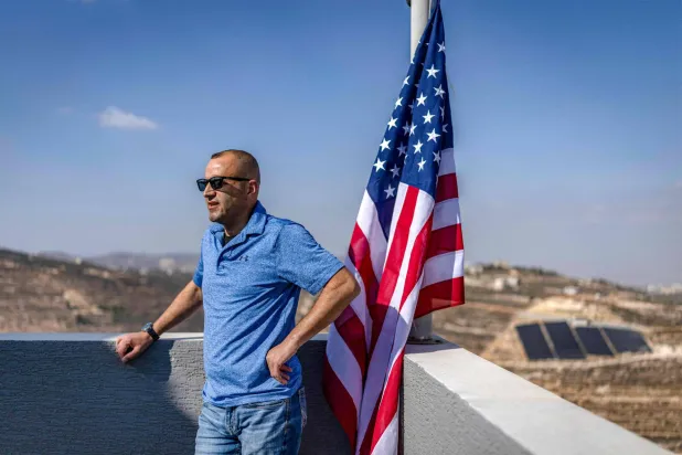 Palestinian-American dual citizen Louai Abu Ridi, whose home in the occupied West Bank village of Qusra is besieged by Israeli settlers, poses for a picture next to a US flag on the roof of the building in Qusra on August 18, 2026. (AFP)