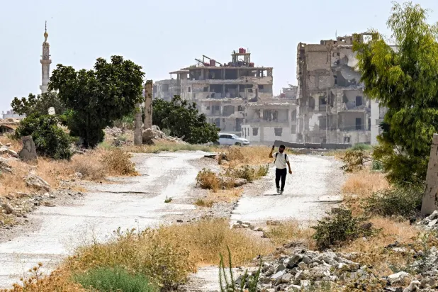 A man walks past heavily-damaged and destroyed buildings in the Jobar suburb northeast of Damascus on August 12, 2026. (Photo by LOUAI BESHARA / AFP)