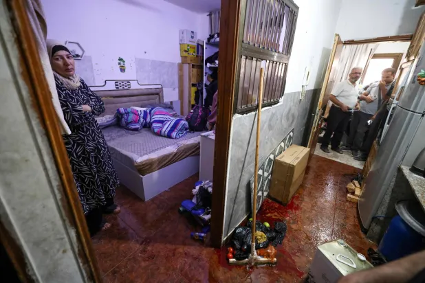 The wife of 58-year-old Fathi Khazem, who was killed by the Israeli military as they tried to arrest him, stands at the bedroom door near a pool of his blood at their home in the northern city of Jenin, in the Israeli-occupied Palestinian West Bank on August 21, 2026. (AFP)