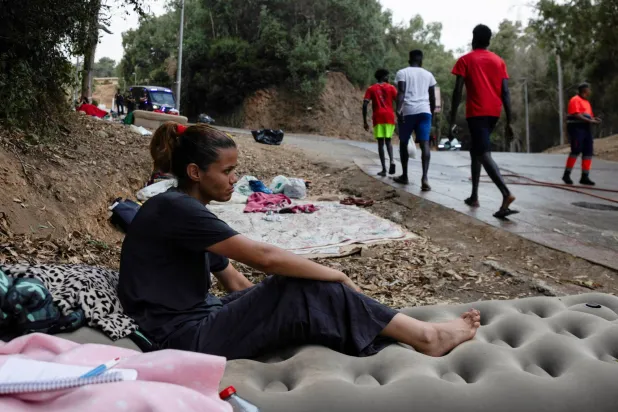 Moroccan migrant Wafae Atid sits on her inflatable mattress as men walk along the road near the Temporary Immigrant Reception Center (CETI) in Ceuta, Spain, August 16, 2026. REUTERS/Maria Alejandra Cardona