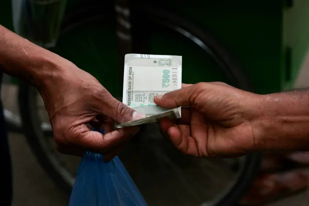 بائع متجول على جانب الطريق يسلم ورقة نقدية لأحد الزبائن في بنغالورو بالهند (رويترز)
