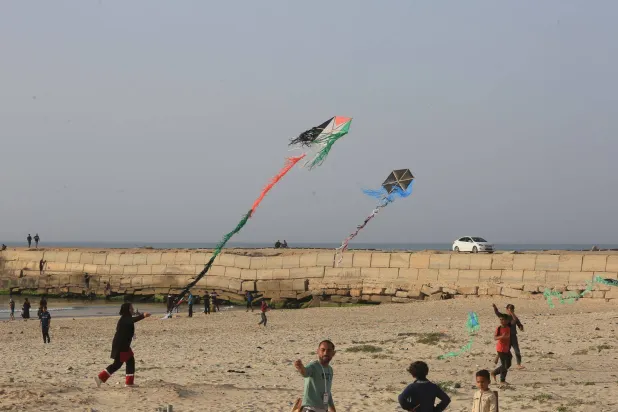 فلسطينيون يشاهدون طائرة ورقية بألوان العلم الفلسطيني خلال فعالية في خان يونس مارس 2024 (د.ب.أ)