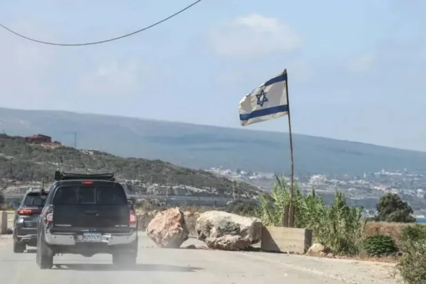 Civilians from Christian villages in southern Lebanon travel south along the coastal road in a convoy, as an Israeli flag is seen at the entrance to Naqoura in July 2026. (File photo/AFP)