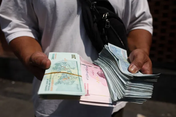 صراف يحمل أوراقاً نقدية من الريال الإيراني في السوق الكبيرة بطهران 17 أغسطس الحالي (رويترز)