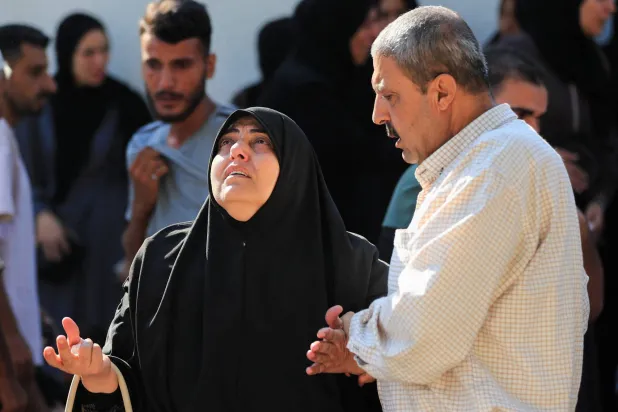 رجل يواسي امرأة ثكلى خلال جنازة فلسطينيين قُتلوا في غارات إسرائيلية في مدينة غزة يوم الأربعاء (رويترز)