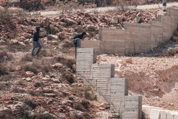 Israeli settlers jump over the garden wall as they make their way towards a Palestinian home under construction in the village of Qusra, south of the city of Nablus in the Israeli-occupied West Bank, which has faced escalating settler violence over the past month, on August 29, 2026. (AFP)