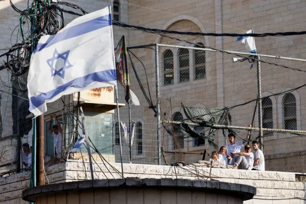  Israeli settlers look out through a metal fence, as an Israeli flag flutters nearby, on the day of their weekly tour in Hebron, in the Israeli-occupied West Bank, August 29, 2026. (Reuters)