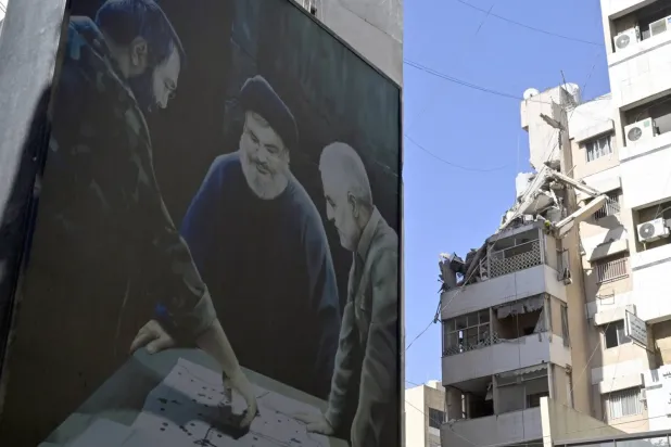 Beyrut’un güney banliyölerinde, Haret Hreik’te İsrail hava saldırısının gerçekleştiği yere yakın bir binada asılı bir pankartta Kasım Süleymani, Hasan Nasrallah ve İmad Muğniye’nin fotoğrafları görülüyor. (Arşiv – EPA)