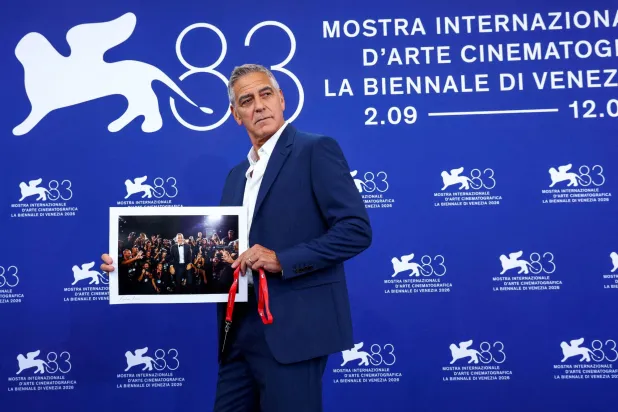 جورج كلوني يرفع صورة له من مهرجان البندقية السينمائي السابق خلال جلسة تصوير في الدورة الثالثة والثمانين لمهرجان البندقية السينمائي في البندقية - إيطاليا 2 سبتمبر 2026 (رويترز)