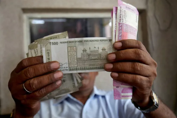 يتحقق أمين صندوق من أوراق نقدية بالروبية الهندية داخل غرفة بمحطة وقود في أحمد آباد (رويترز)