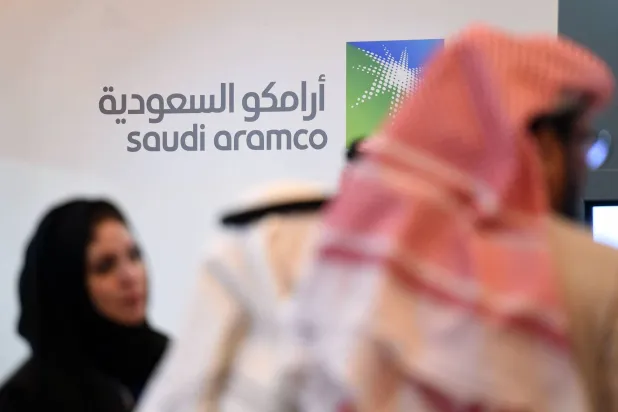 أشخاص يقفون أمام شعار شركة «أرامكو» خلال المنتدى العالمي العاشر للتنافسية (أرشيفية - أ.ف.ب)