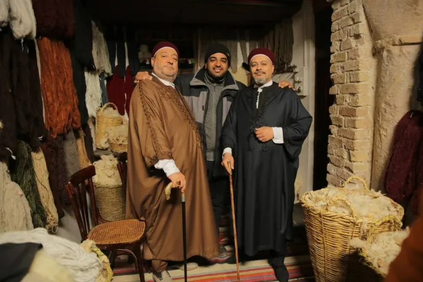 المخرج الليبي أسامة رزق يتوسط الفنانين كافو (إلى اليسار) ومحمد عثمان خلال تصوير مسلسل «زنقة الريح» عام 2019 (الشرق الأوسط)