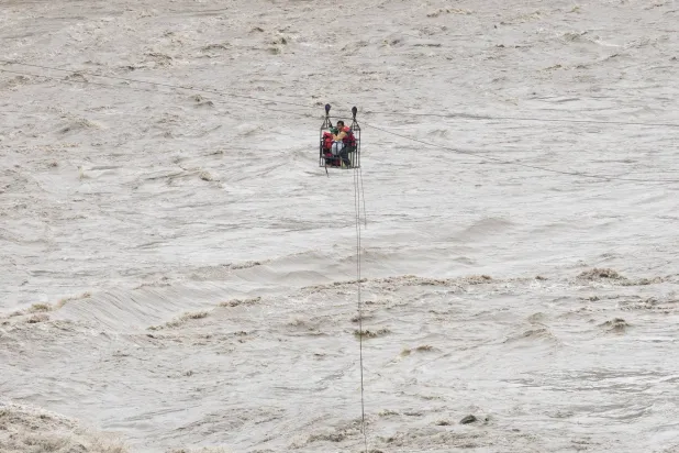 People hold onto a cage on a makeshift zip line as they cross the Trishuli River from Koloni following deadly flash floods that damaged bridges and temporarily stranded residents, in Nuwakot district, Nepal, September 4, 2026. REUTERS/Adnan Abidi
