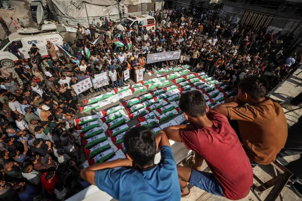 تَجمَّع المشيّعون في مدينة غزة لدفن جماعي لنحو 100 فلسطيني بينهم 62 طفلاً انتُشل رفاتهم من تحت الأنقاض (أ.ف.ب)