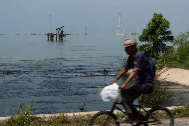 A man rides a bicycle in front of abandoned oil wells in Maracaibo lake, Zulia state, Venezuela on September 7, 2026. (Photo by John Chacَn / AFP)