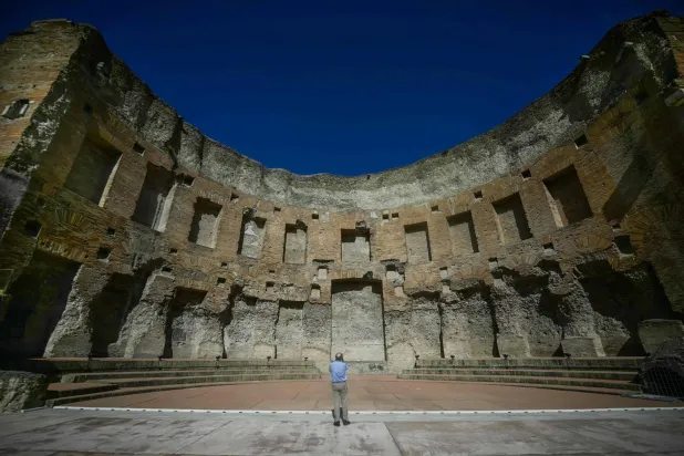 A visitor views the restored south-western exedra of the Baths of Trajan, a monumental second-century AD hall believed to have served as a library or space for public readings, with the Colosseum seen in the background, in Rome on September 8, 2026. (AFP)