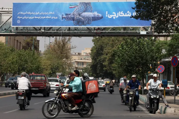 إيرانيون يمرون أمام لوحة دعائية في طهران تُظهر مسيّرة أميركية تحت الماء قال «الحرس الثوري» إنه استولى عليها وتحمل عبارة «صيد الصياد» 9 سبتمبر 2026 (إ.ب.أ)