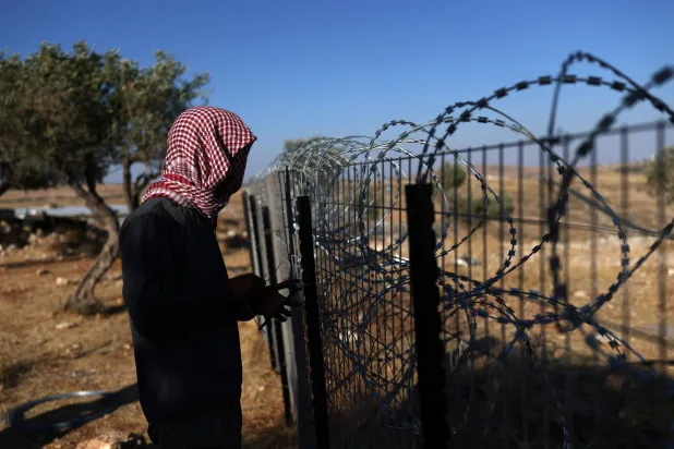 فلسطيني يعزز سياجاً حول بيته بقرية الطيبة في الضفة الغربية يوم الأربعاء لمنع هجمات المستوطنين (إ.ب.أ)