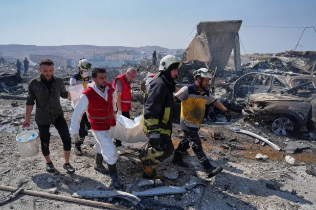 عناصر الدفاع المدني ورجل إطفاء ينتشلون جثة من موقع انفجار مستودع للتخزين المؤقت للأسلحة بالقرب من سرمدا بمحافظة إدلب الأربعاء (أ.ب)