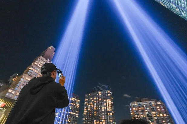 A person takes a photo of the "Tribute in Light" public art installation commemorating the 9/11 2001 terrorist attacks as it shines up from the skyline of lower Manhattan in preparation for the 25th anniversary, in New York City, on September 10, 2026. (AFP)