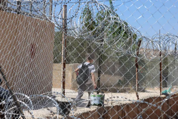 صبي فلسطيني يغادر المدرسة ويظهر خلف سياج أمني يحيط بساحة المدرسة في قرية المغير قرب رام الله بالضفة الغربية (إ.ب.أ)