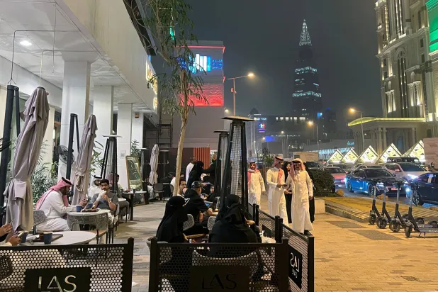 يمر الناس أمام مقهى على طول شارع التحلية التجاري في الرياض (أ.ف.ب)