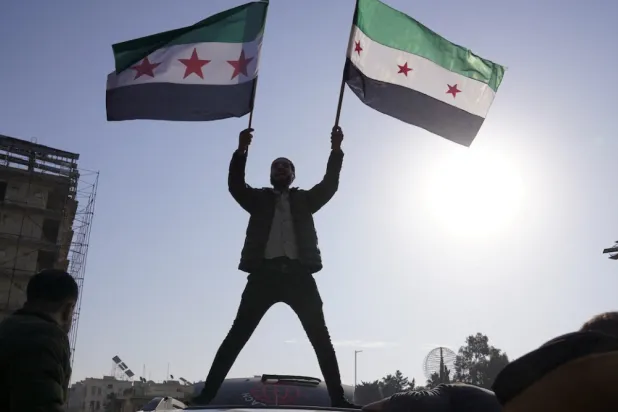 A man holds Syrian opposition flags as he celebrates after Syria's army command notified officers that President Bashar al-Assad's 24-year authoritarian rule has ended, in Aleppo, Syria December 8, 2024. REUTERS/Karam al-Masri
