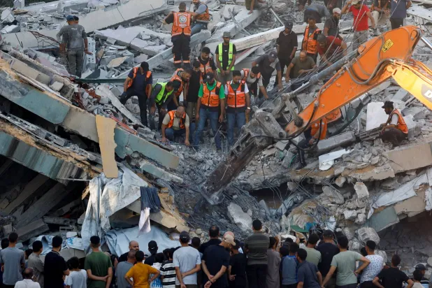 أشخاص يتجمعون فيما يحاول عناصر الدفاع المدني إنقاذ الأشخاص العالقين تحت أنقاض مبنى منهار في مدينة غزة الأربعاء (رويترز)