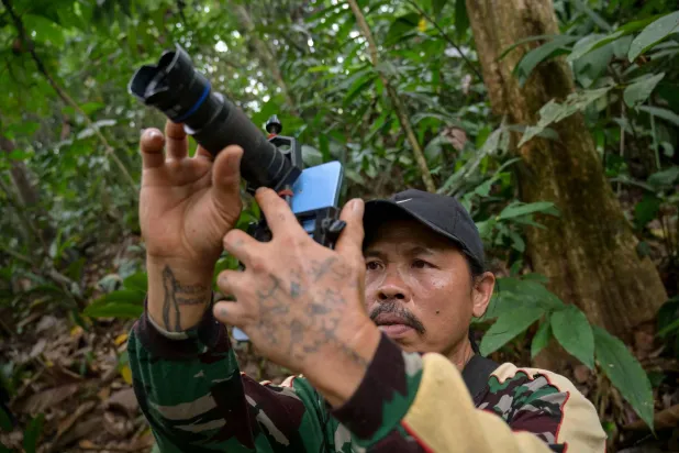This picture taken on September 2, 2026 shows wildlife observer and former poacher Octavius using a mobile phone equipped with a telephoto lens to take pictures of wildlife in a forest near Labian village in Kapuas Hulu, West Kalimantan. (Photo by BAY ISMOYO / AFP)