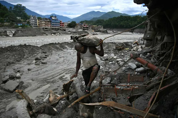 A man carrying his belongings walks past a damaged house in the aftermath of flash floods at Trishuli in Nepal's Nuwakot district on September 11, 2026. (Photo by Prakash MATHEMA / AFP)