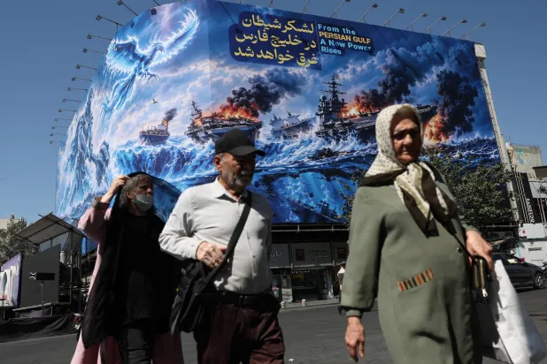 أشخاص يسيرون أمام لوحة إعلانية تتناول موضوع مضيق هرمز مثبتة على مبنى في طهران (رويترز)