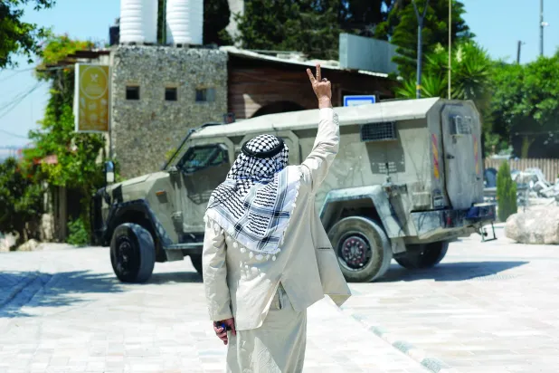 مستوطنون وجنود إسرائيليون يقفون بحقل في حين يُمنع المزارعون الفلسطينيون من قطف الزيتون بقرية سعير قرب مدينة الخليل بالضفة الغربية (أرشيفية - أ.ف.ب)