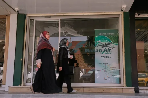 İran hava yolu şirketi Mahan Air’in Bağdat’taki ofisinin önünden geçen yayalar (AP)