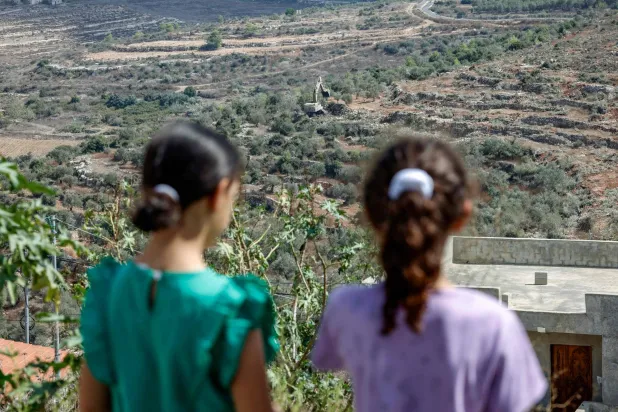 فتيات فلسطينيات يشاهدن جرافة إسرائيلية تقتلع أشجار الزيتون في قرية دير نظام شمال غرب رام الله في الضفة الغربية المحتلة (أ.ف.ب)