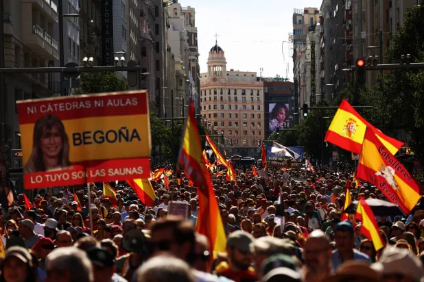 متظاهرون في مدريد يحملون الأعلام وصورة لبيغونيا زوجة رئيس الوزراء المتهمة بالفساد (رويترز)