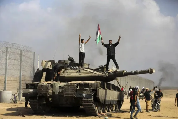 فلسطينيون يحتفلون على ظهر دبابة إسرائيلية على الجدار العازل قرب خان يونس في جنوب قطاع غزة يوم 7 أكتوبر 2023 (أ.ب)