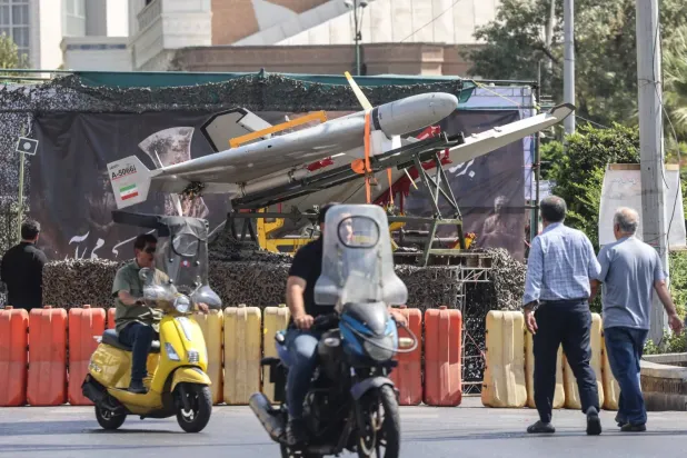 İranlılar, pazartesi günü Tahran'daki Baharistan Meydanı'nda sergilenen askeri İHA'ların önünden motosikletleriyle geçiyor (AFP)
